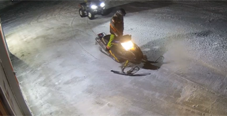 Snowmobile moving across snow, headlights illuminate the scene