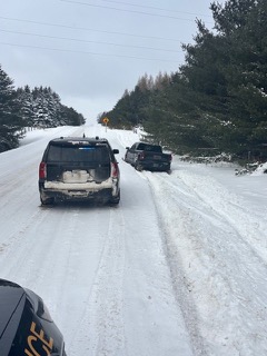 Snow-covered road with two SUVs, one police vehicle, visible.