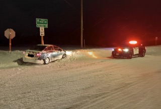 Damaged red car and police vehicle in snow.