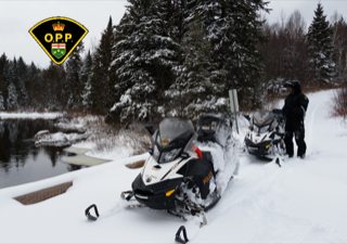 Snowmobile partially submerged in water, police officer standing nearby