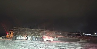 Logging truck hauling logs on a snowy road at night