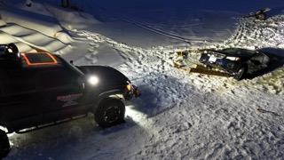 Black pickup truck with winch and plow, stuck in deep snow.