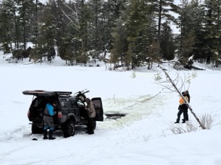 Black SUV in snow, two people in orange vests