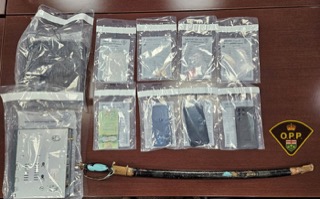 Several clear plastic bags containing what appear to be drugs. A black pipe with a blue mouthpiece. O.P.P. logo in the upper right corner.