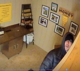 Man in a black hoodie and black bandana stands in a honey shop.